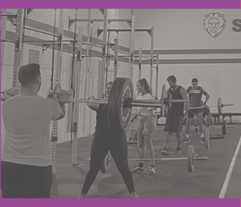 Una clase de Salvaje entrenando con barras bajo el rótulo del box